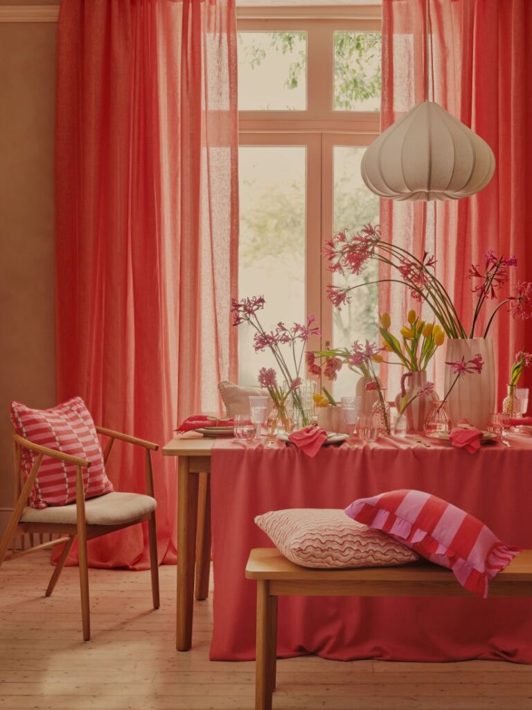 Coral sheer curtains and dining table with lots of flowers in vases.